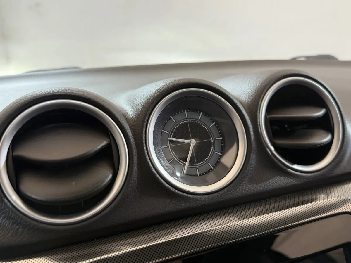 Gros plan sur l'horloge ronde et les aérateurs noirs cerclés d'argent du tableau de bord du Suzuki Vitara noir.