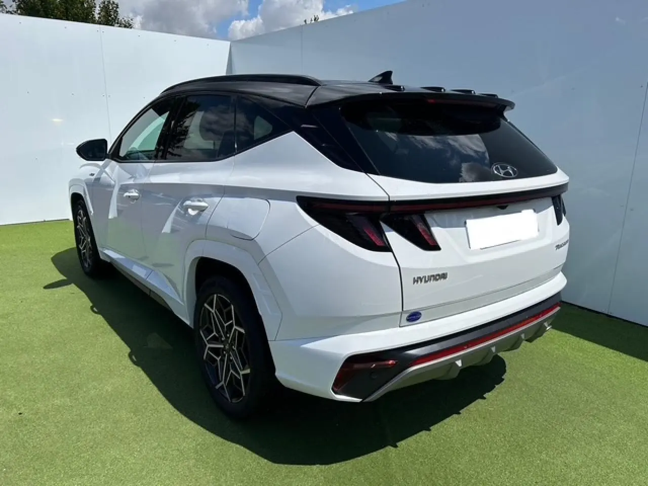 Vue 3/4 arrière droite du Hyundai Tucson blanc polaire avec toit noir et détails N-LINE visibles sur pare-chocs et jantes.