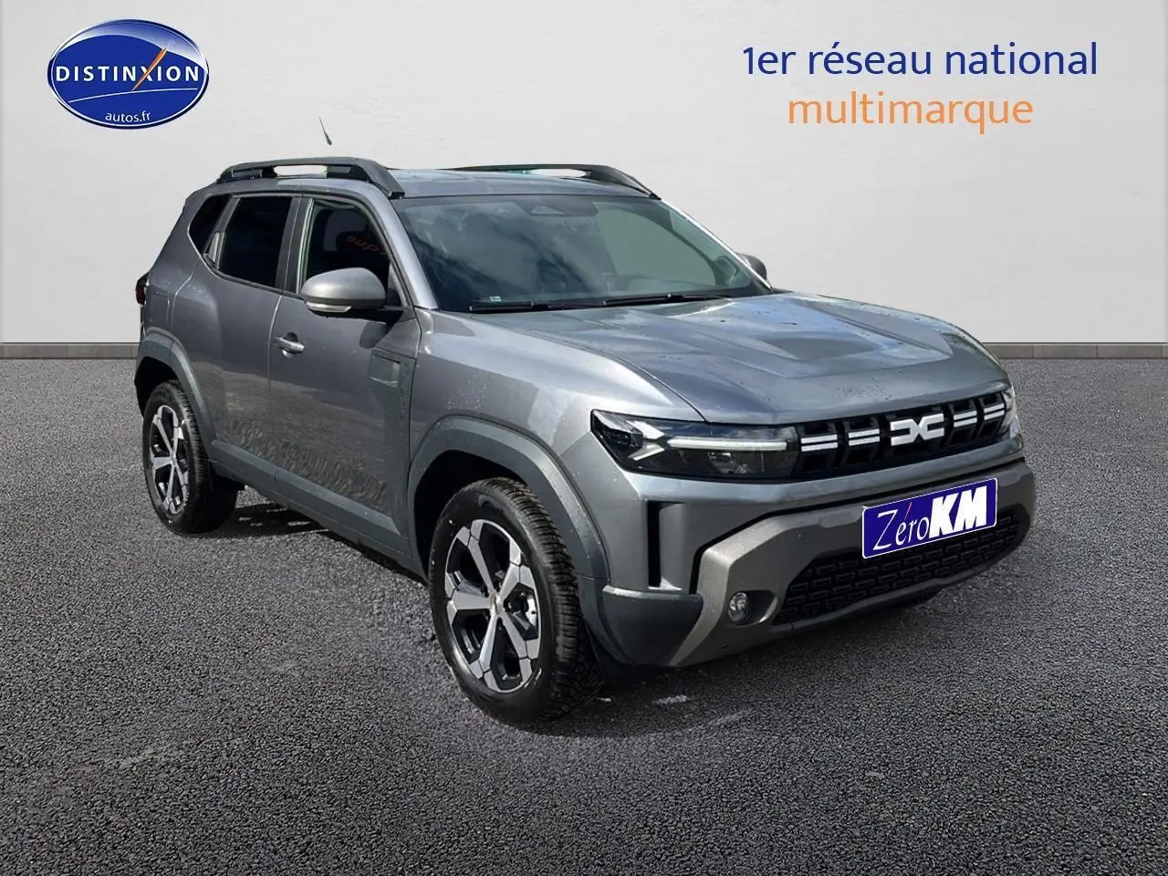 Dacia Duster gris schiste en 3/4 avant droit, avec barres de toit et jantes alu distinctives.