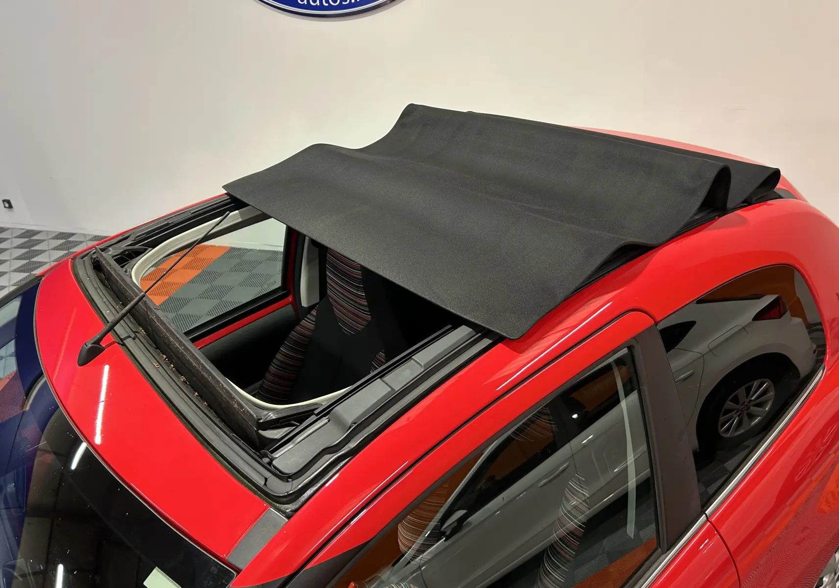 Vue plongeante sur l'avant gauche d'une Citroën C1 rouge 3 portes avec toit ouvrant en toile partiellement déployé.