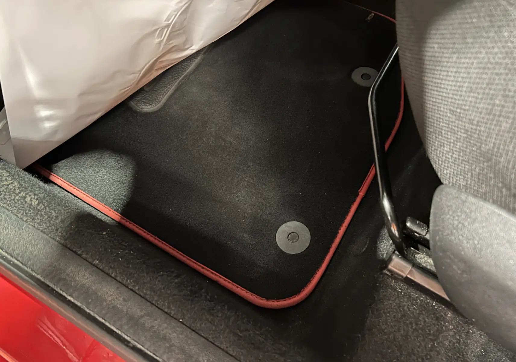 Vue rapprochée du tapis de sol noir avec bordure rouge côté conducteur d'une Citroën C1 rouge 2019.