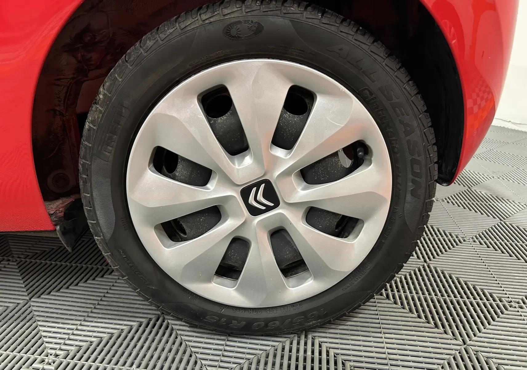 Gros plan sur la roue avant gauche d'une Citroën C1 rouge de 2019, avec enjoliveur argenté et logo Citroën central.