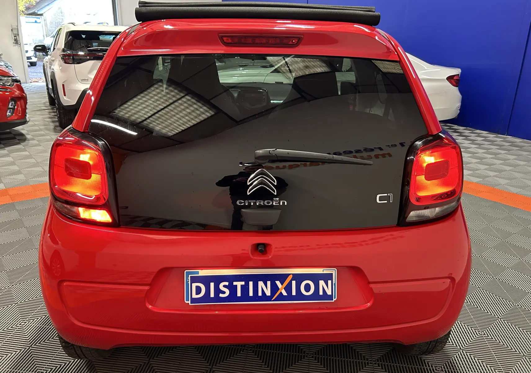 Vue arrière d'une Citroën C1 rouge avec hayon noir brillant et feux arrière allumés dans un garage.