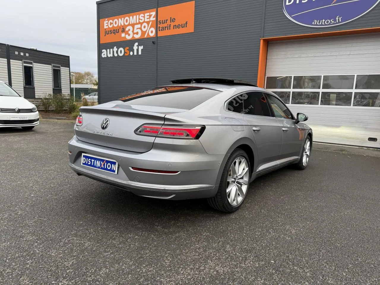 Vue 3/4 arrière droite d'une Volkswagen Arteon gris pyrite métallisé avec jantes alliage 19 pouces devant un garage.