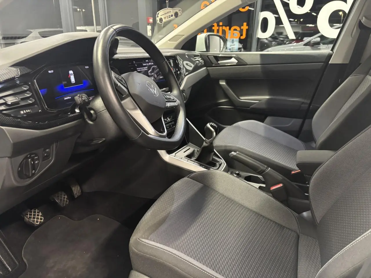 Vue intérieure côté conducteur du Volkswagen Taigo 2023, montrant le volant cuir multifonctions et la sellerie tissu grise.