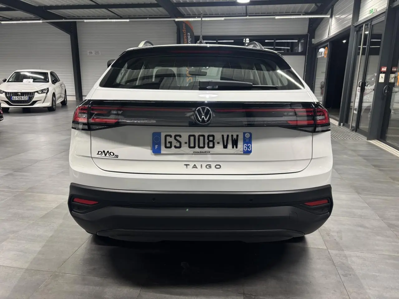 Vue arrière d'un Volkswagen Taigo blanc 2023 en intérieur avec feux arrière reliés par une bande noire brillante.
