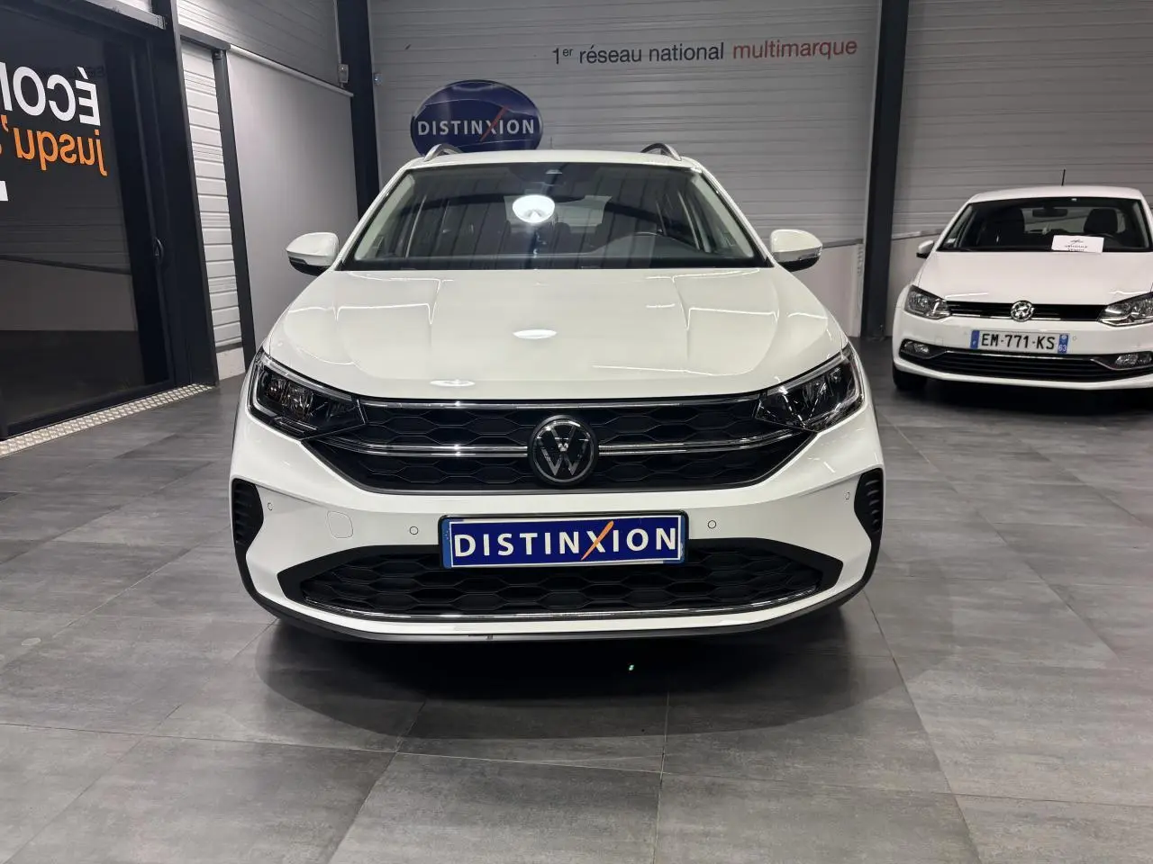 Vue avant d'un Volkswagen Taigo blanc 2023 avec calandre noire et logo VW central dans un showroom.
