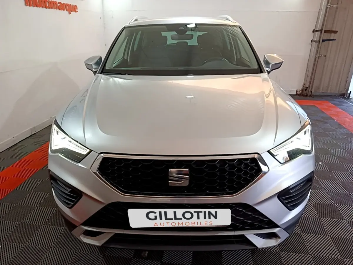 Vue avant d'un SEAT Ateca gris clair avec calandre hexagonale noire et phares LED allumés dans un garage.