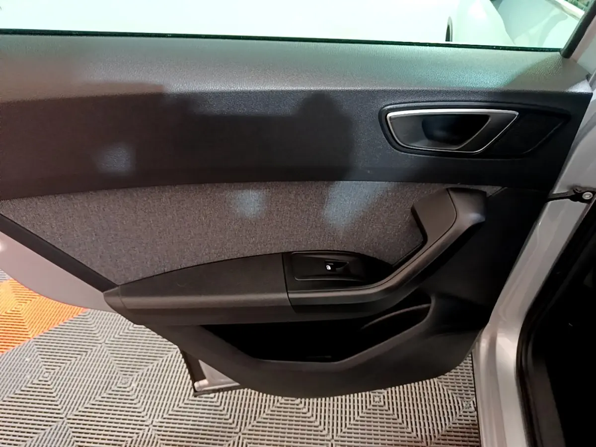 Vue intérieure côté gauche de la porte avant d’un SEAT Ateca gris clair, avec poignée noire et panneau tissu gris.