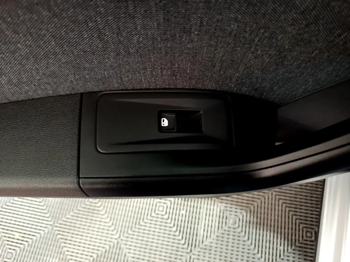 Gros plan sur le bouton d'ouverture électrique du coffre, situé sur le côté intérieur d'une SEAT Ateca gris clair.