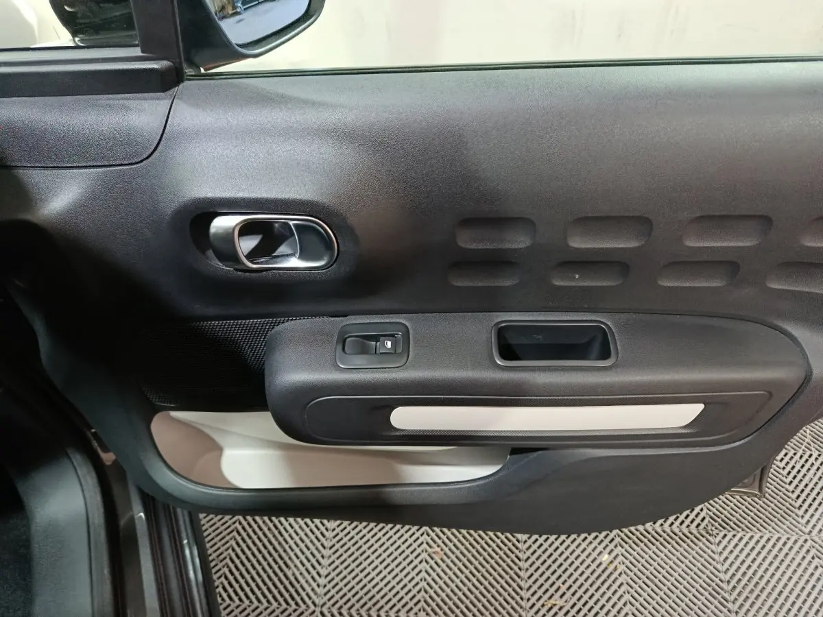 Vue rapprochée de la porte côté conducteur de la Citroën C3 gris foncé, avec poignée intérieure et commande de vitre.