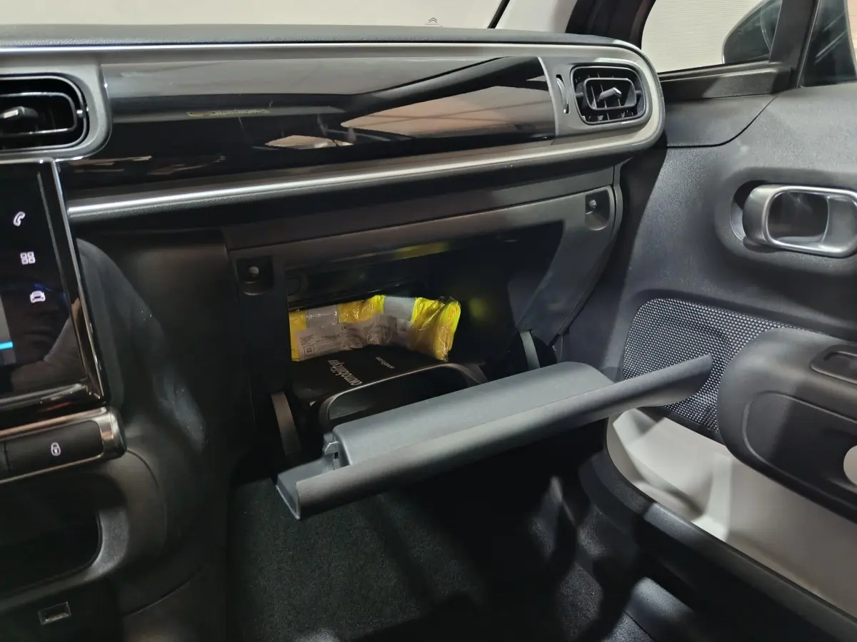 Vue intérieure côté passager du coffre à gants ouvert d'une Citroën C3 2024 gris foncé, avec tableau de bord noir brillant.