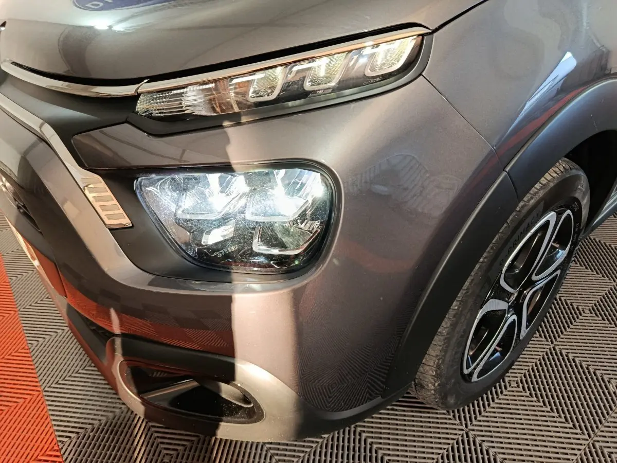 Gros plan sur l'avant droit gris foncé du Citroën C3 2024, mettant en valeur ses phares LED et la jante stylisée.