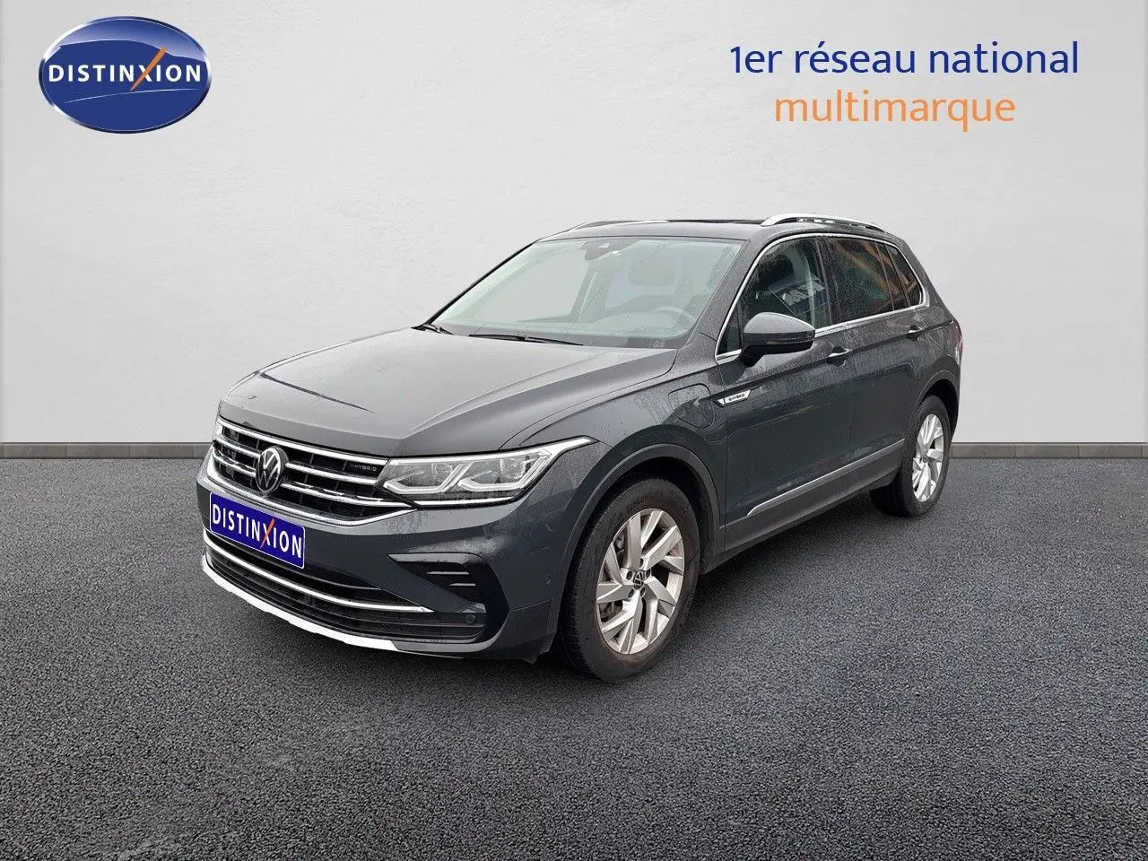 Volkswagen Tiguan 1.4 E-Hybrid gris lunaire en 3/4 avant droit sur sol gris devant un mur blanc.