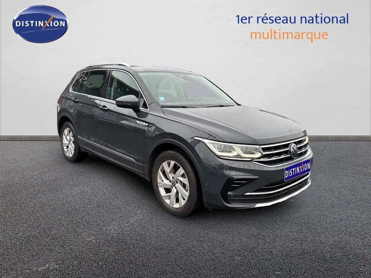 Volkswagen Tiguan 1.4 E-Hybrid gris lunaire vu en 3/4 avant droit avec phares LED allumés sur fond neutre.