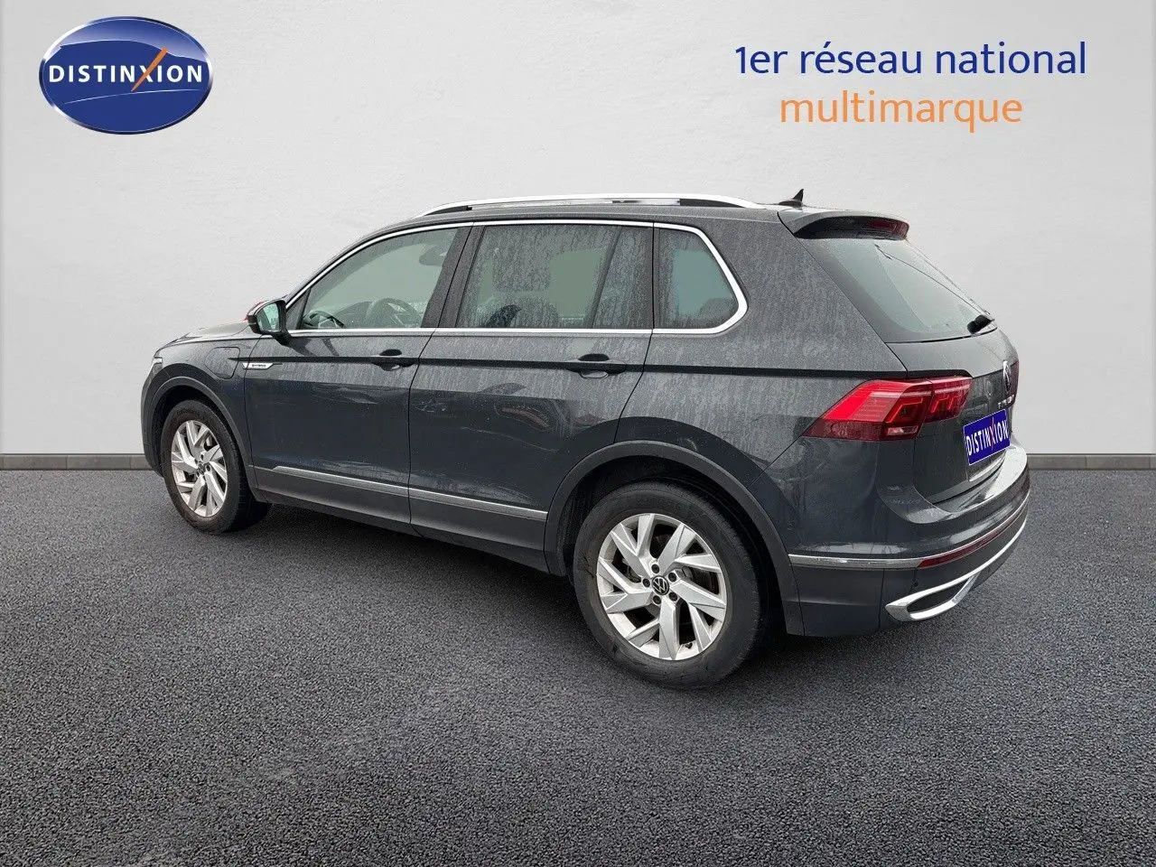 Vue 3/4 arrière côté gauche d'un Volkswagen Tiguan gris lunaire hybride rechargeable de 2022 avec jantes alliage.