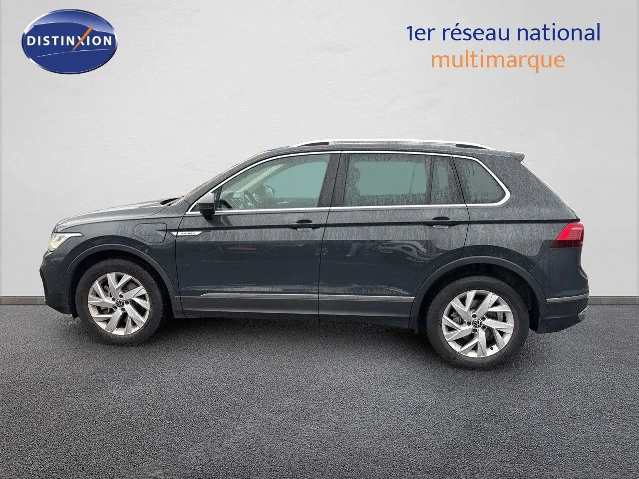 Profil côté gauche d'un Volkswagen Tiguan 1.4 e-Hybrid gris lunaire, avec jantes alliage et toit ouvrant visible.