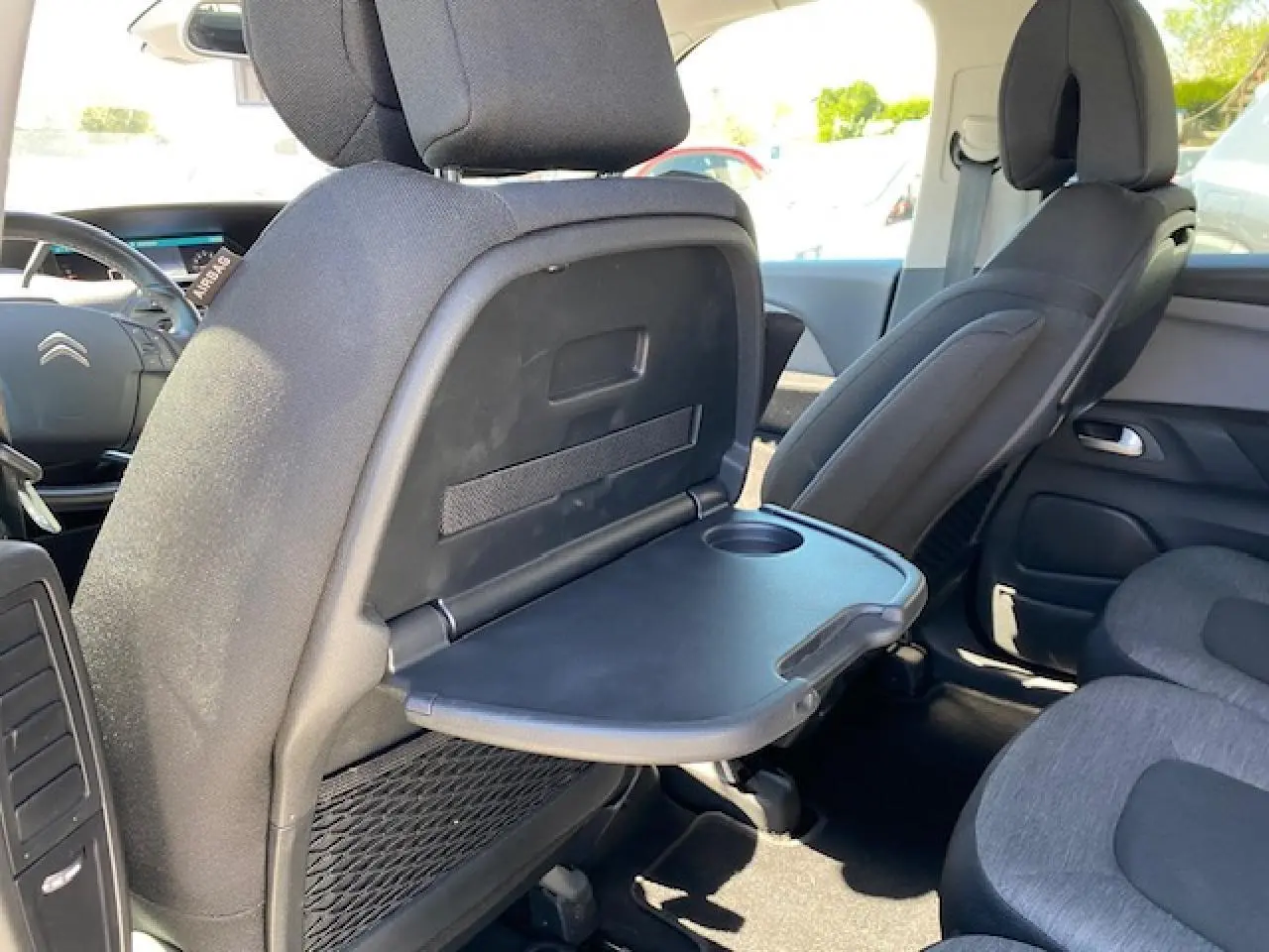 Vue intérieure arrière droite du Citroën C4 Picasso 2016 gris Shark, tablette rabattable avec porte-gobelet sur siège avant.