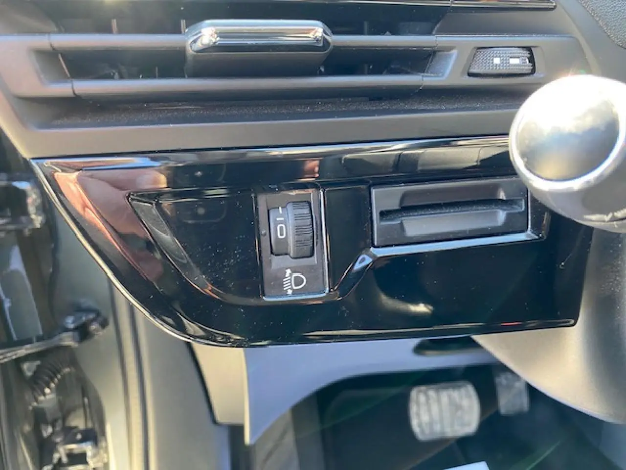 Gros plan sur la commande de réglage des phares côté gauche du tableau de bord intérieur d'une Citroën C4 Picasso gris shark.