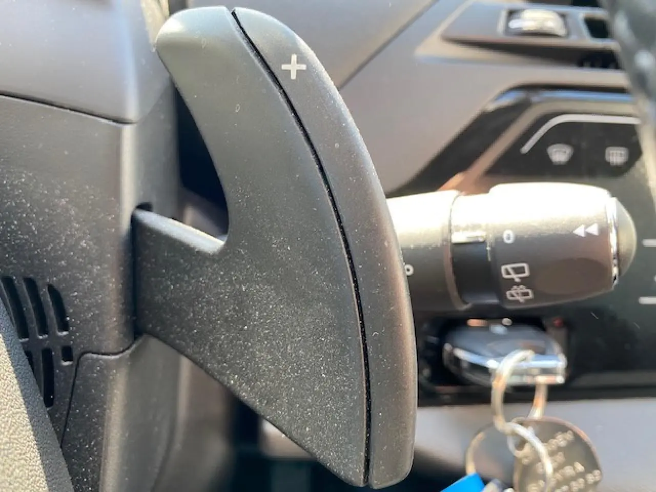 Gros plan sur la palette de commande + au volant noir du Citroën C4 Picasso 2016, avec clé insérée au contacteur.