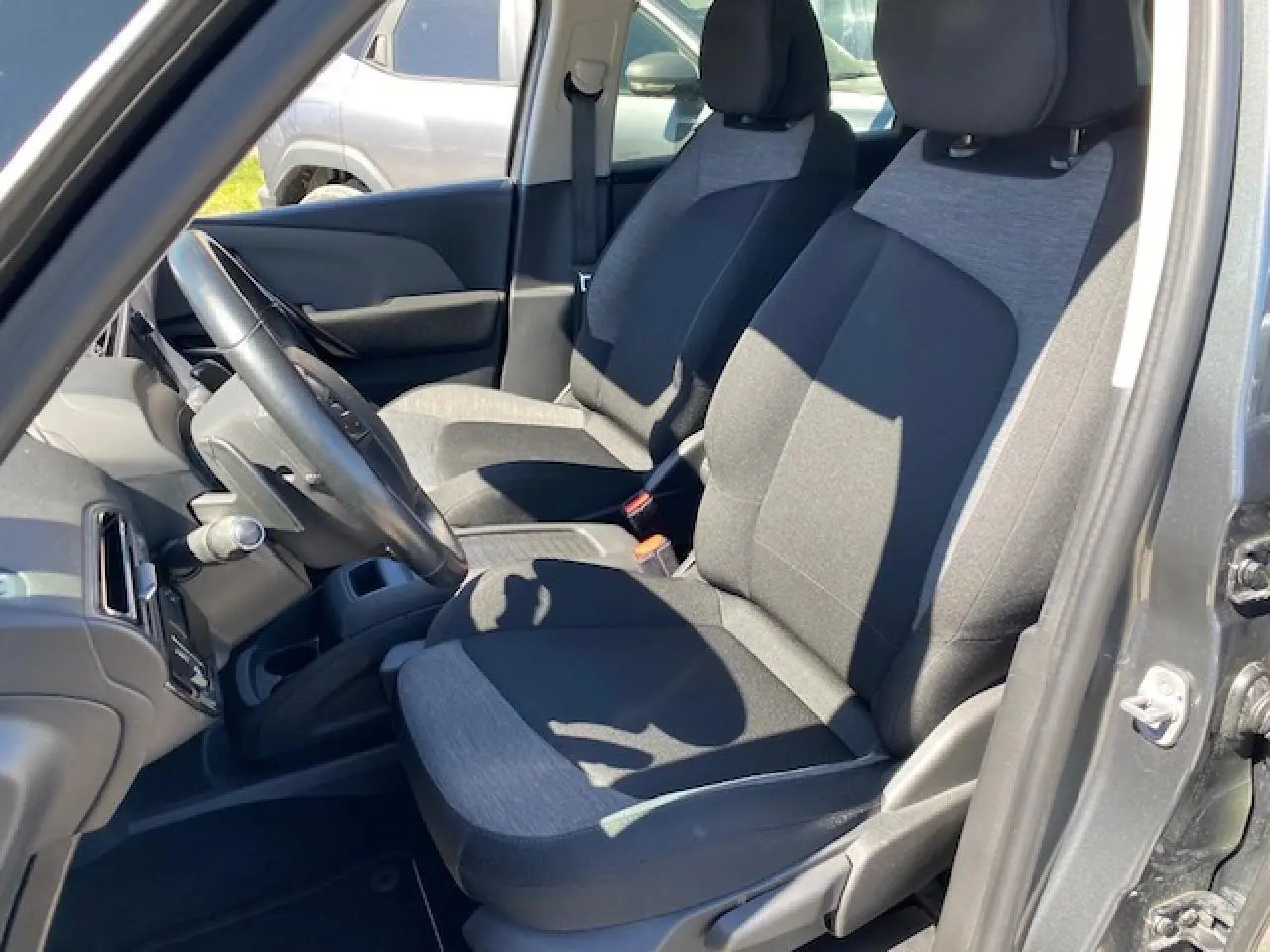 Vue intérieure côté conducteur de la Citroën C4 Picasso gris shark, sièges tissu bicolore noir et gris, volant cuir visible.