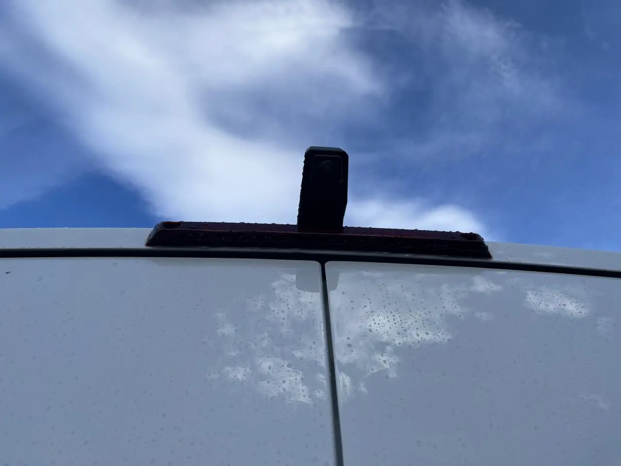 Vue rapprochée de la caméra de recul sur la porte arrière blanche du Renault Master 2025 sous un ciel bleu.