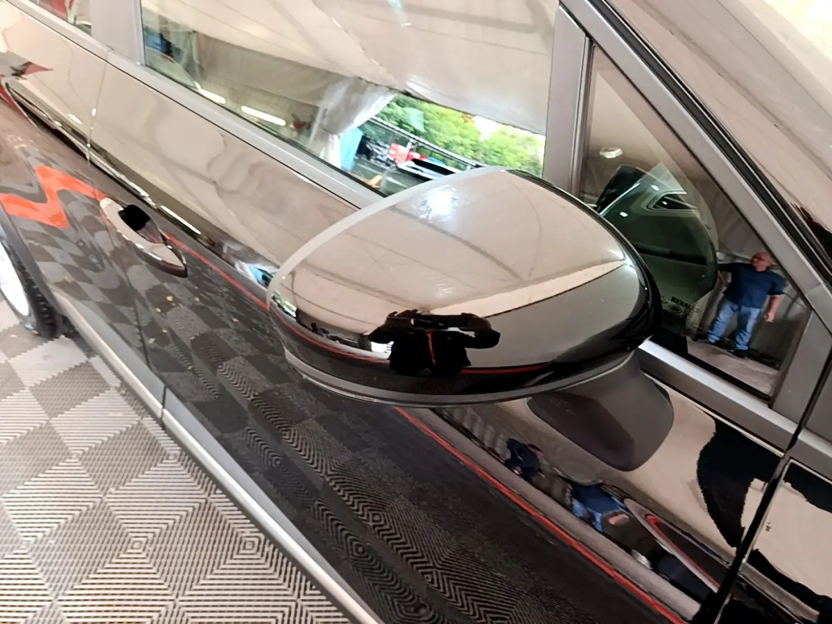 Gros plan sur le rétroviseur côté gauche d'un Renault Captur Business noir brillant, reflet d'un homme visible sur la carrosserie.