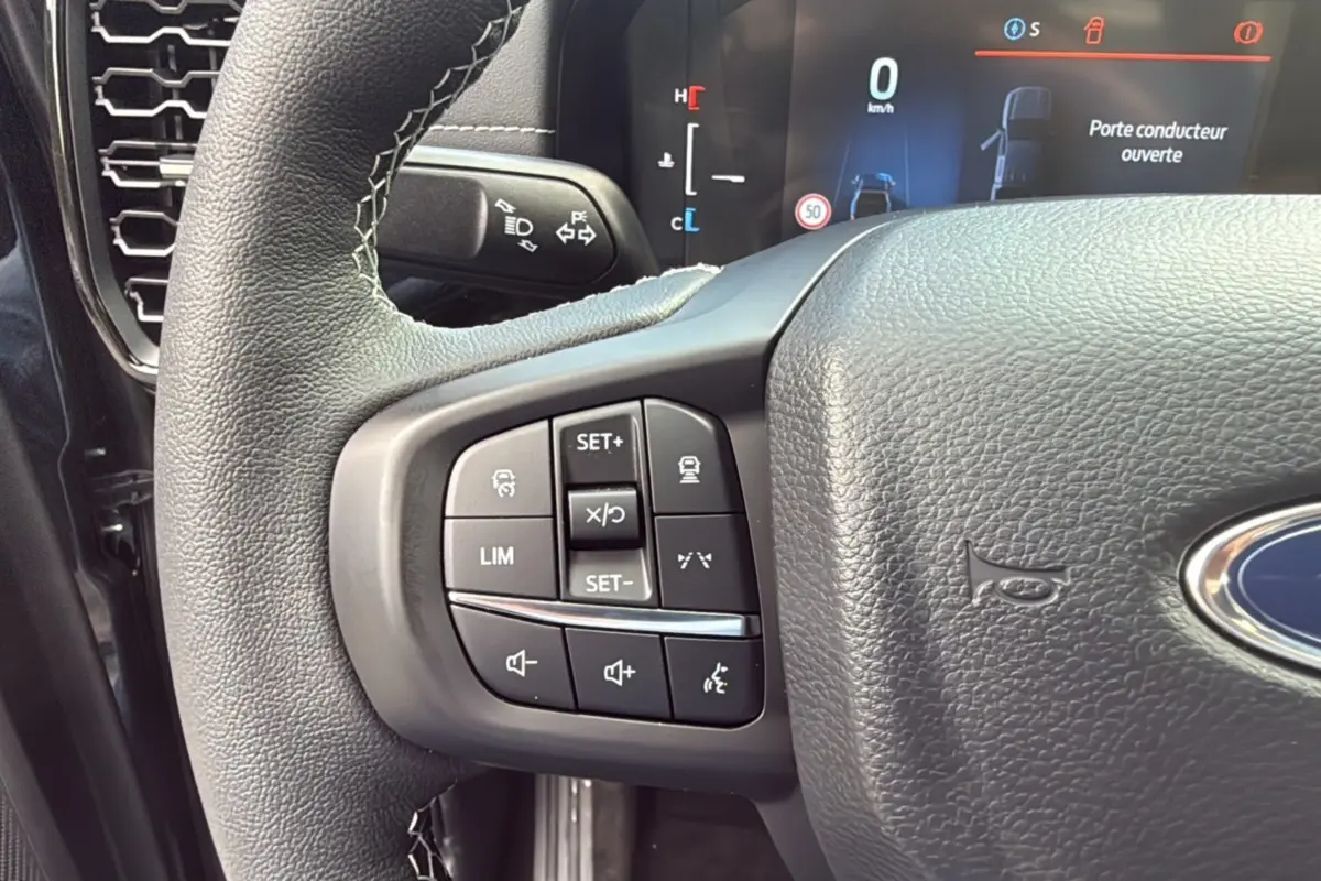 Gros plan sur le volant côté gauche du Ford Ranger 2025 noir agate, avec commandes intégrées et tableau de bord numérique visible.