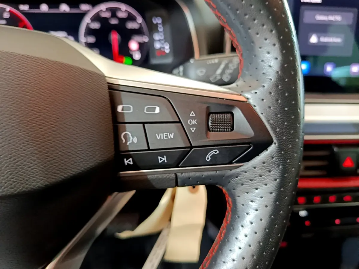 Gros plan sur la partie droite du volant en cuir perforé avec surpiqûres rouges du SEAT Arona 2022, boutons multifonctions visibles.