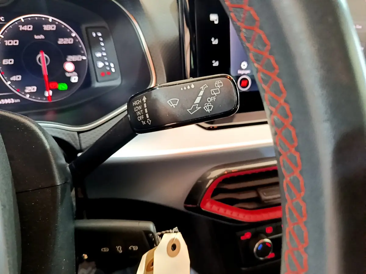 Gros plan sur la commande d’essuie-glace à gauche du volant cuir noir avec surpiqûres rouges, tableau de bord digital visible.