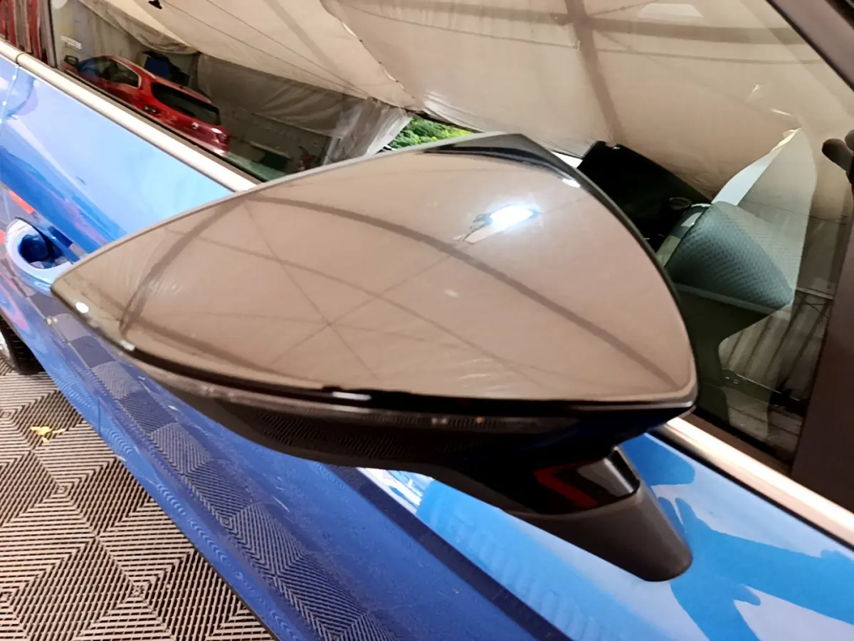 Gros plan sur le rétroviseur noir du côté gauche d’un SEAT Arona bleu 2022, avec reflet de la tente au-dessus.