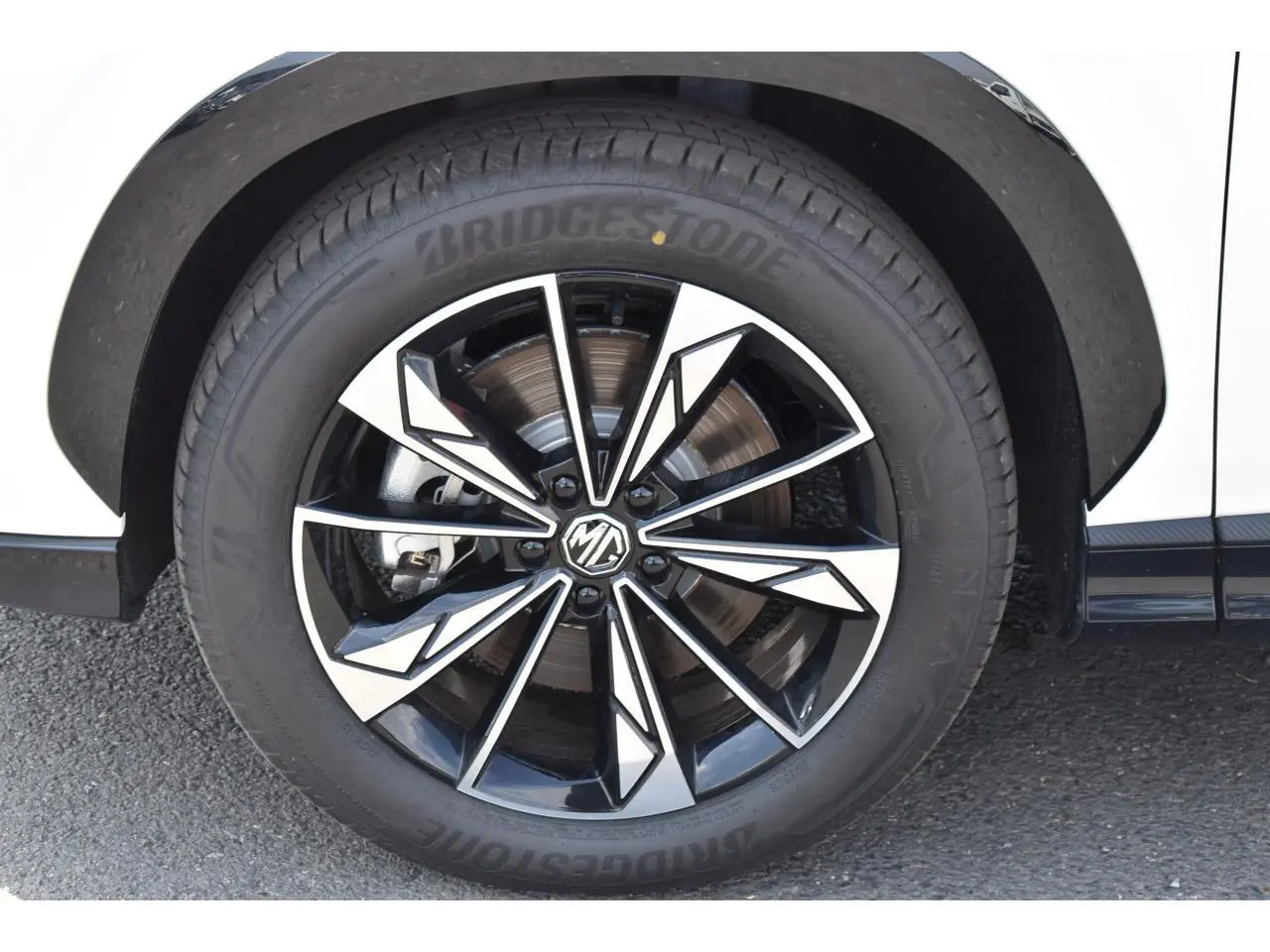 Gros plan sur la jante alliage 19 pouces bicolore du MG MOTOR EHS blanc, avec pneu Bridgestone visible côté droit.