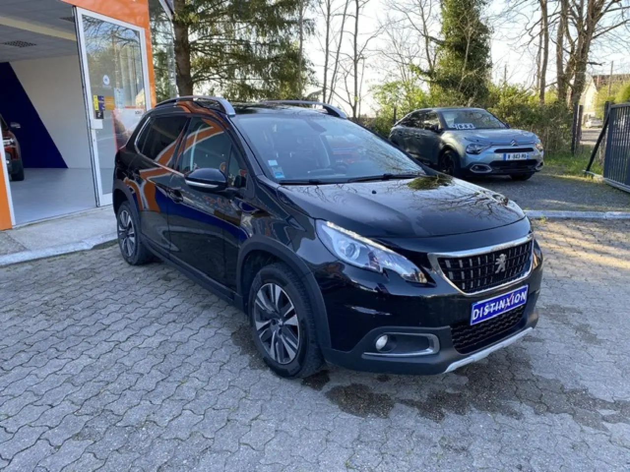 Peugeot 2008 noir métallisé vue 3/4 avant droit avec jantes aluminium 16 pouces et calandre distinctive.