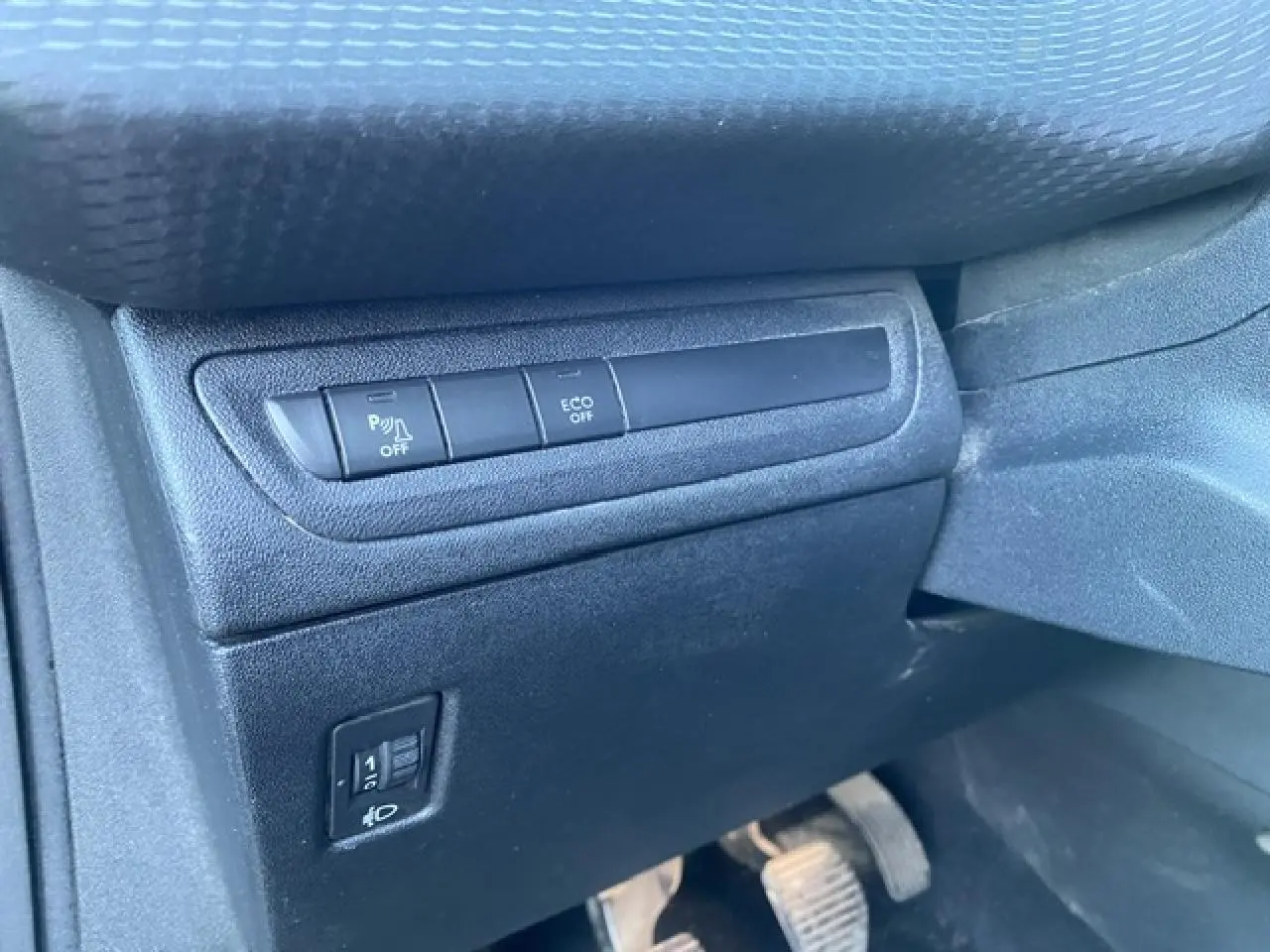 Vue rapprochée des commandes d'aide au stationnement et d'économie d'énergie sur le tableau de bord côté conducteur d'une Peugeot 2008 noire.