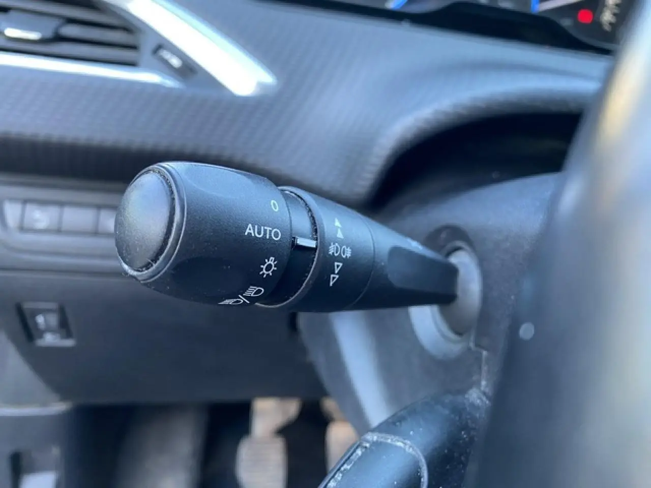 Gros plan sur la commande d'éclairage à gauche du volant dans l'habitacle d'un Peugeot 2008 noir de 2019.