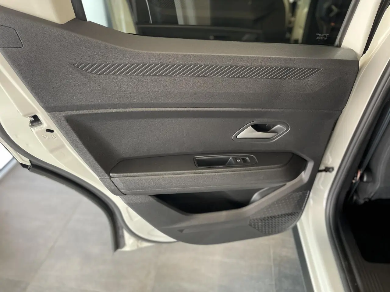 Porte arrière gauche ouverte du Dacia Duster beige 2025, montrant la garniture intérieure noire avec commandes de fenêtre.