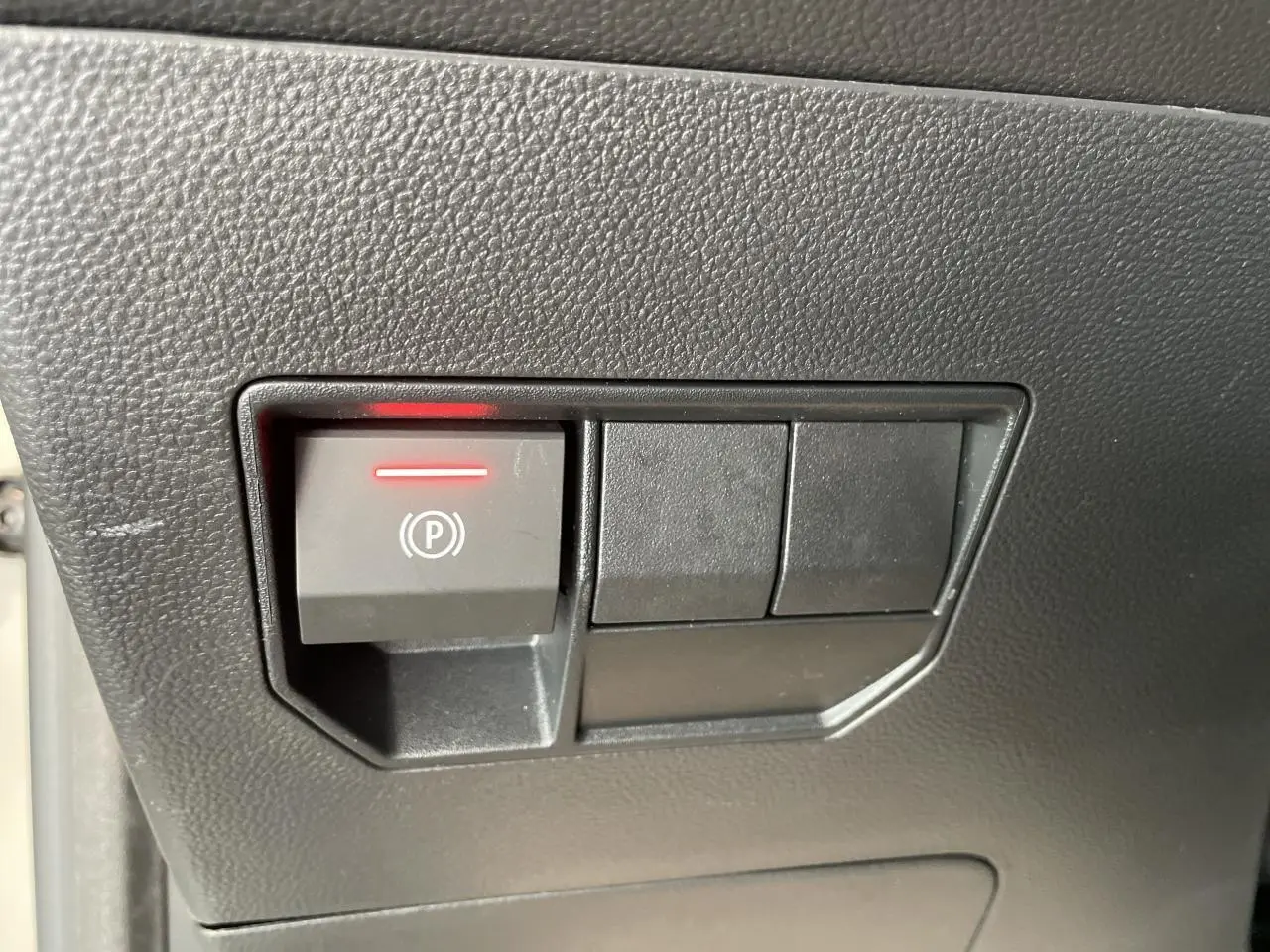 Gros plan sur le bouton de frein de stationnement électrique allumé dans l'habitacle du Dacia Duster beige.