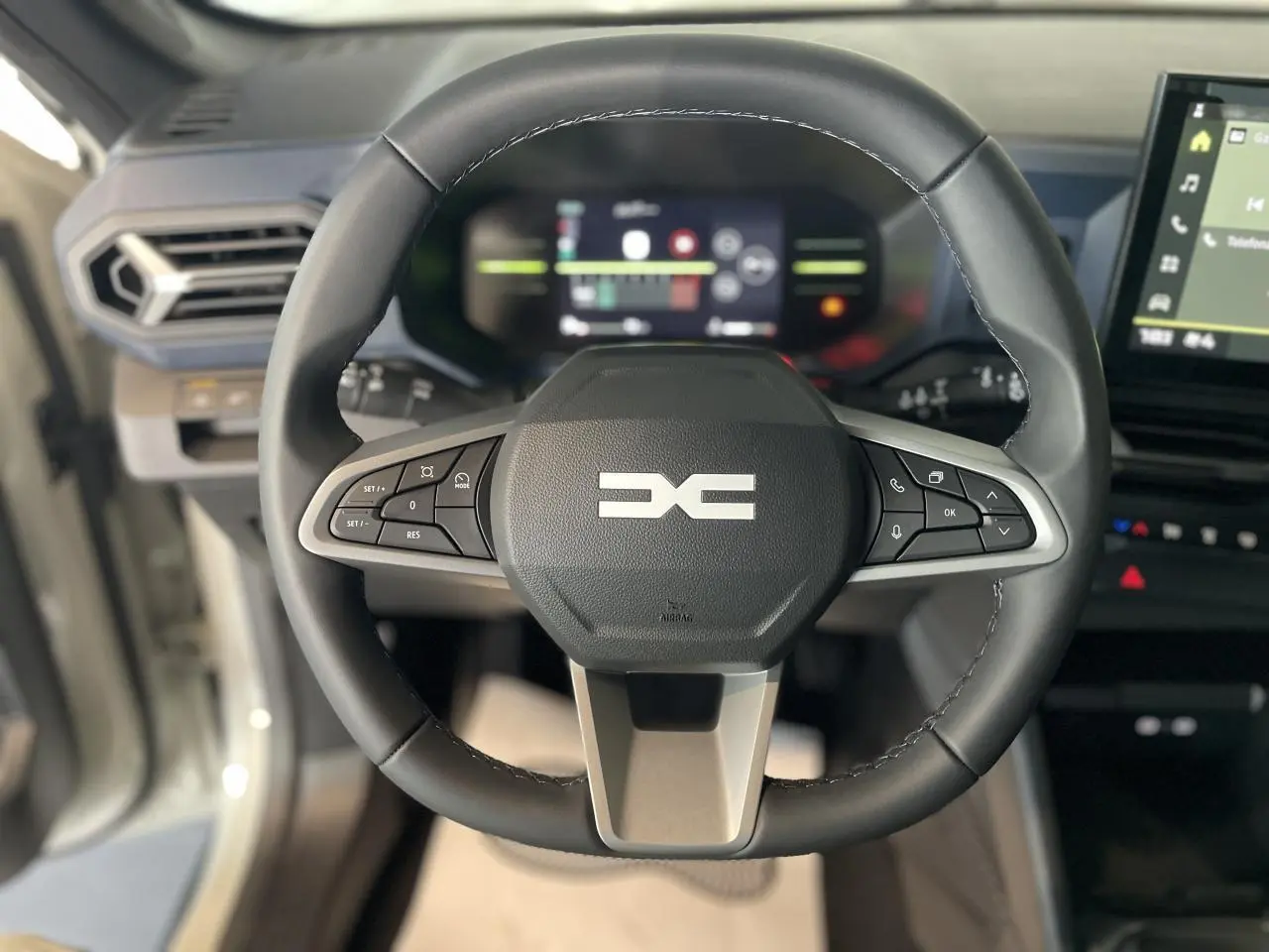 Vue rapprochée du volant noir du Dacia Duster 2025 avec commandes intégrées et tableau de bord digital flou en arrière-plan