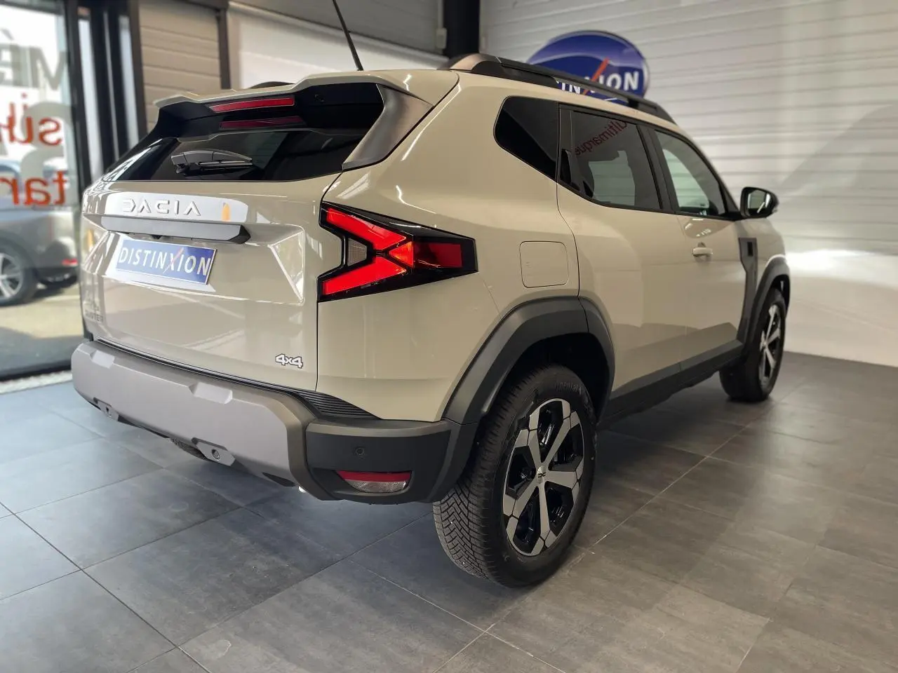 Vue 3/4 arrière droit du SUV Dacia Duster beige avec jantes alliage 18 pouces et barres de toit noires.