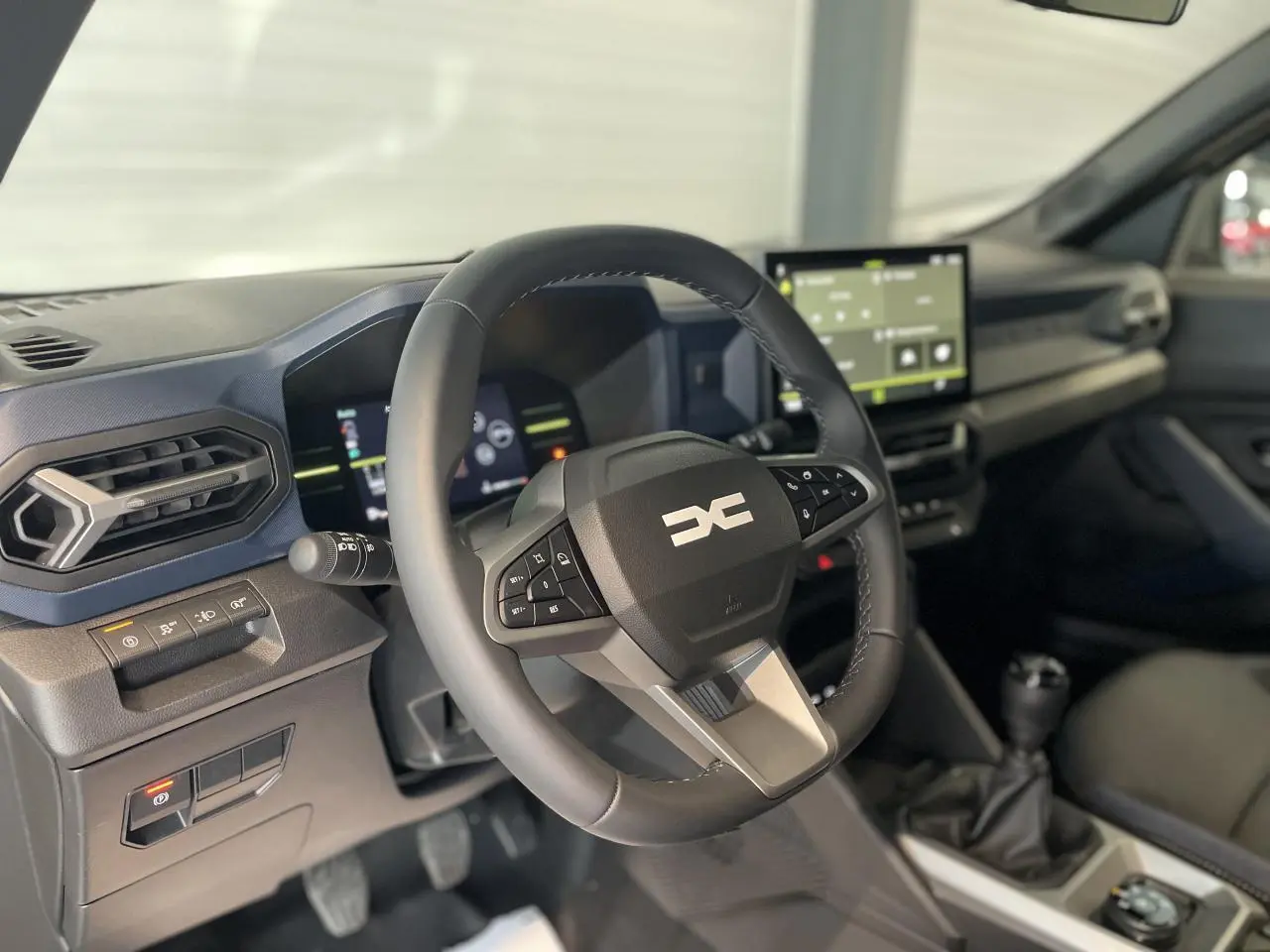 Vue intérieure centrée sur le volant et la console centrale du Dacia Duster 2025 avec boîte manuelle et écran tactile.