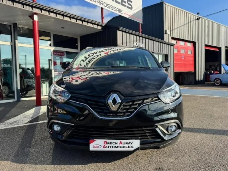 Vue frontale d'un Renault Grand Scenic noir étoilé garé devant un garage avec logo Renault bien visible sur la calandre.