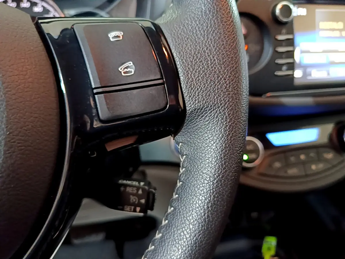 Gros plan sur le volant cuir noir de la Toyota Yaris hybride 2020 avec commandes intégrées et tableau de bord flou en arrière-plan.