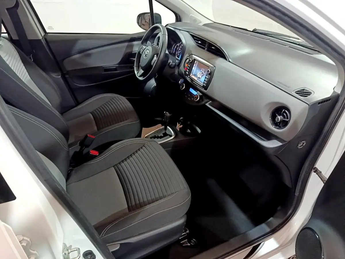 Vue intérieure côté conducteur de la Toyota Yaris blanche 2020, montrant sièges noirs et tableau de bord avec écran tactile.