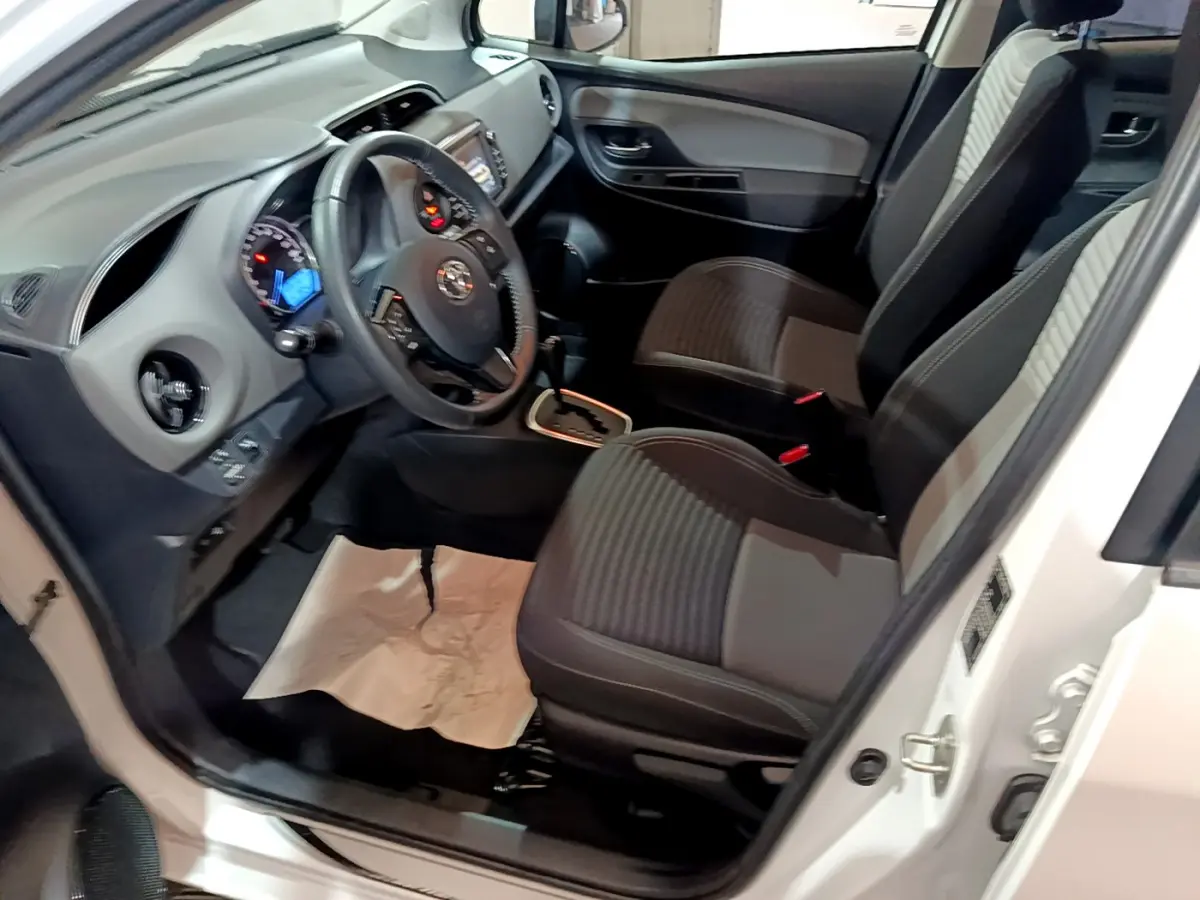 Vue intérieure côté conducteur de la Toyota Yaris blanche 2020, montrant sièges et tableau de bord avec volant multifonction.