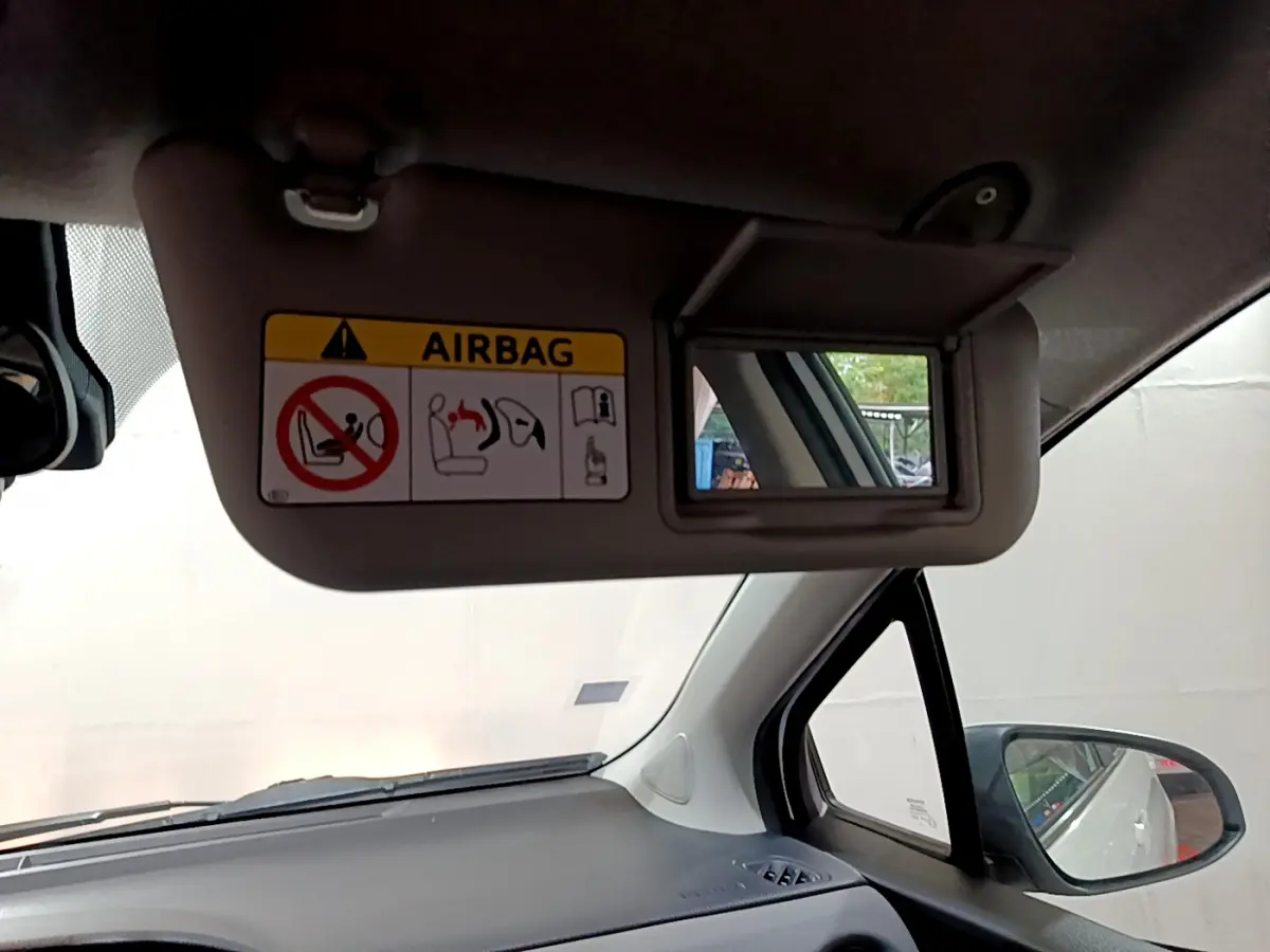 Détail intérieur du pare-soleil côté conducteur de la Toyota Yaris blanche, avec miroir et avertissement airbag visible.