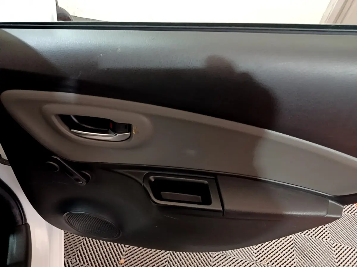 Vue intérieure côté gauche de la porte avant d'une Toyota Yaris blanche, avec poignée chromée et panneau noir et gris.