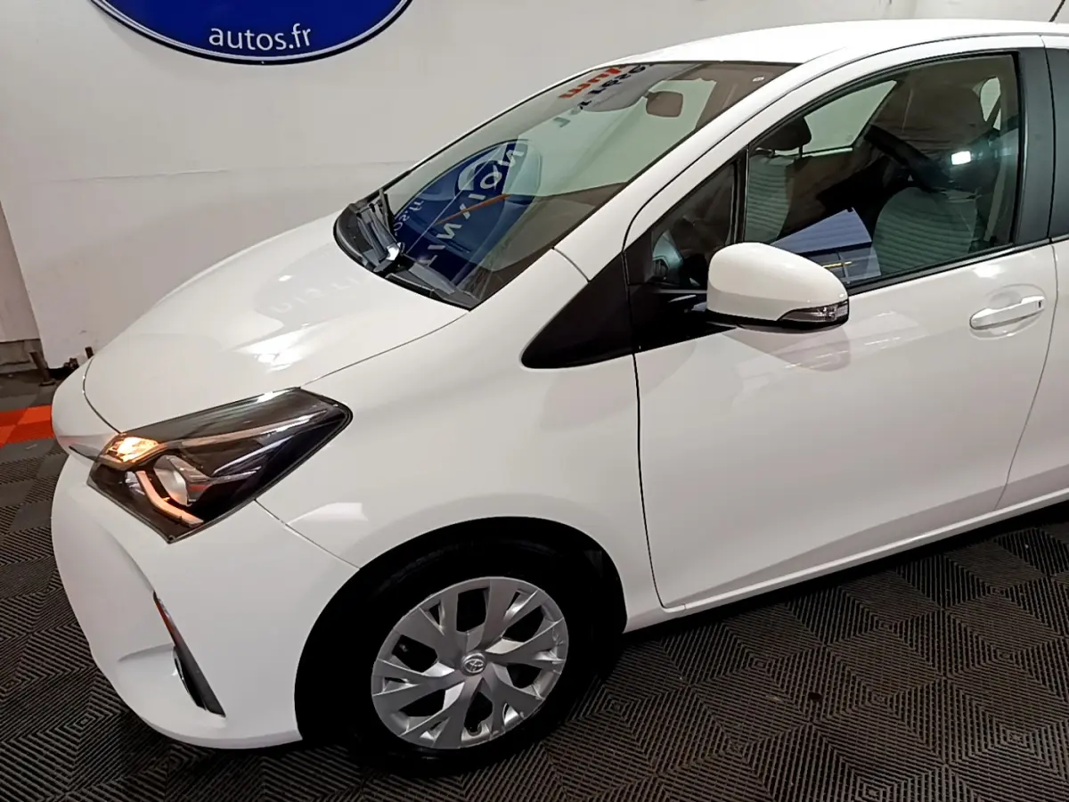Vue 3/4 avant droit d'une Toyota Yaris blanche 2020 avec phares allumés et rétroviseur blanc.