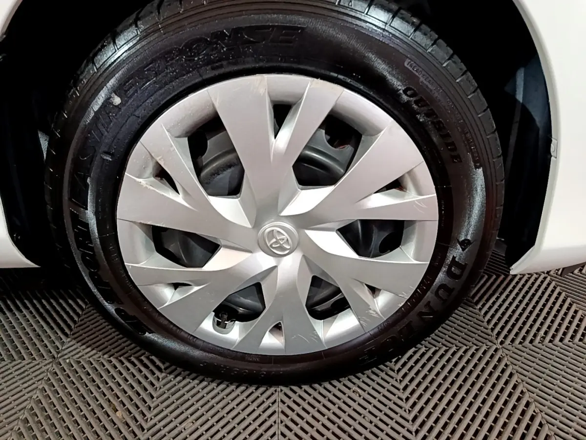 Gros plan sur la roue avant droite d'une Toyota Yaris blanche, jante avec enjoliveur argenté et pneu Dunlop.