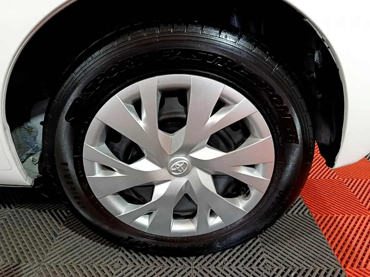 Gros plan sur la roue avant droite d'une Toyota Yaris blanche, avec enjoliveur argenté et pneu Dunlop.