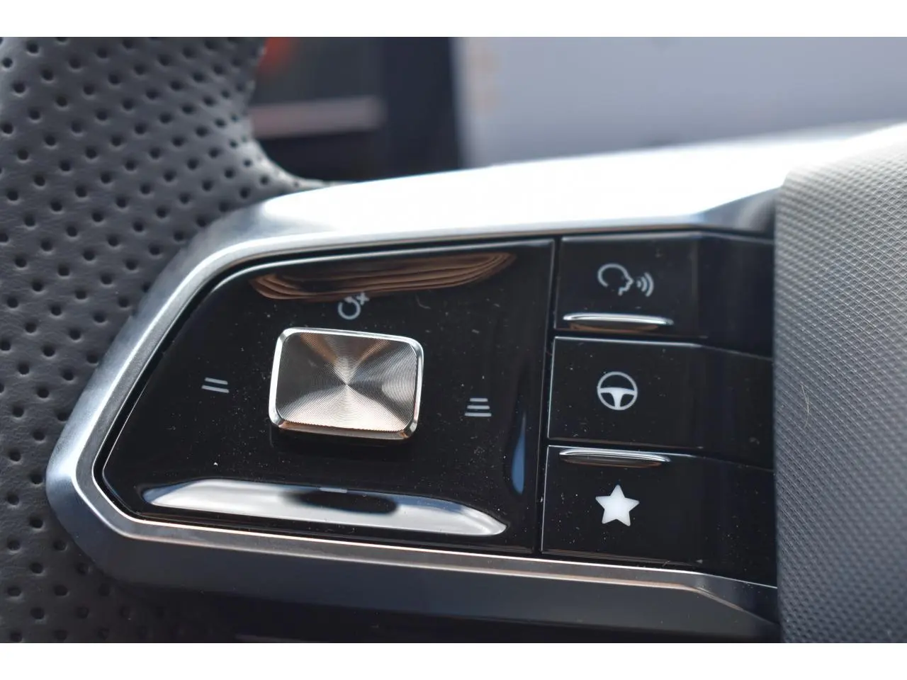 Gros plan sur les commandes multifonctions en plastique noir et chrome du volant perforé du MG MOTOR EHS gris hybride 2026.
